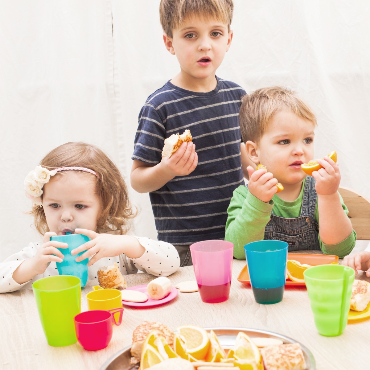 Gesunde Ernährung in der Kita Nordmännchen – bunt, lecker & kindgerecht 🍎 Drei Kleinkinder sitzen gemeinsam am Frühstückstisch in der Kita Nordmännchen. Sie essen frisches Obst und Brot, trinken aus bunten Bechern – fröhliche Esskultur.