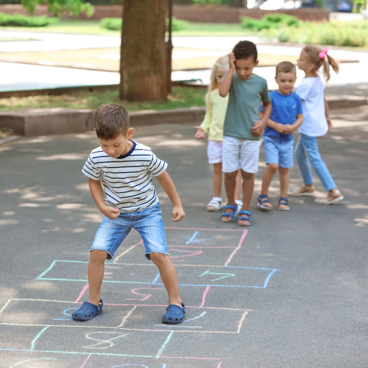 Spielplatzspaß in der Kita Roländchen – Bewegung im Grünen 🌳 Kinder spielen auf einem asphaltierten Hof mit Hüpfspiel in der Kita Roländchen. Fröhliches Toben an der frischen Luft – fördert Motorik und Sozialverhalten.