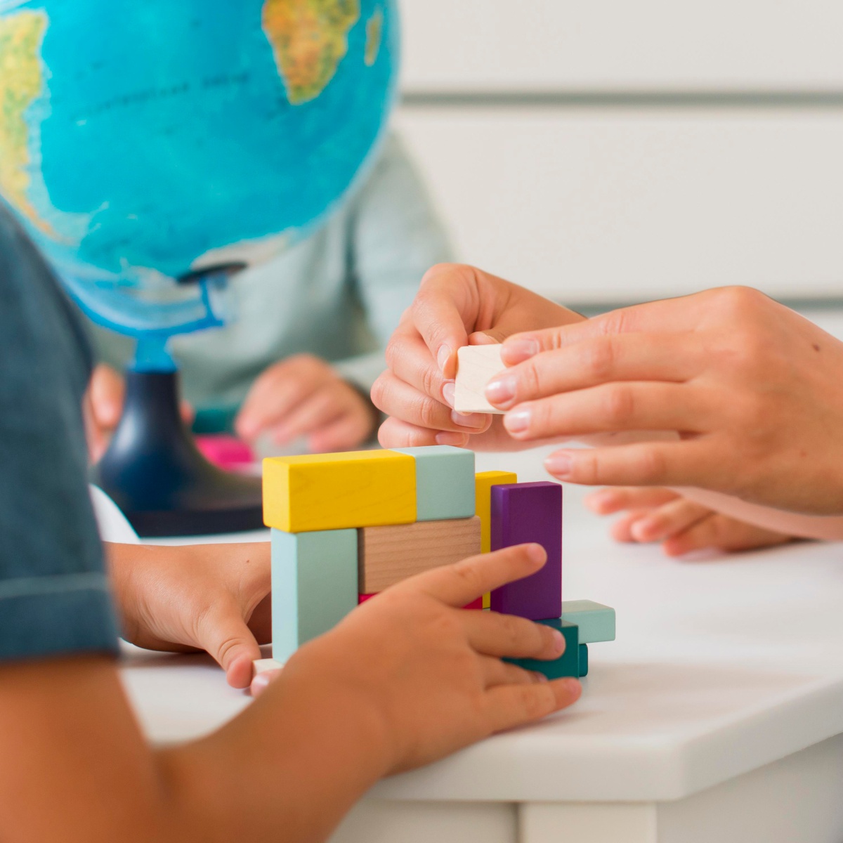 Fördernde Spielzeit in der Kita Roländchen – kreatives Lernen 🧠 Kinder bauen mit bunten Holzbausteinen unter Anleitung einer Erzieherin in der Kita Roländchen. Im Hintergrund: Globus, Lernatmosphäre.