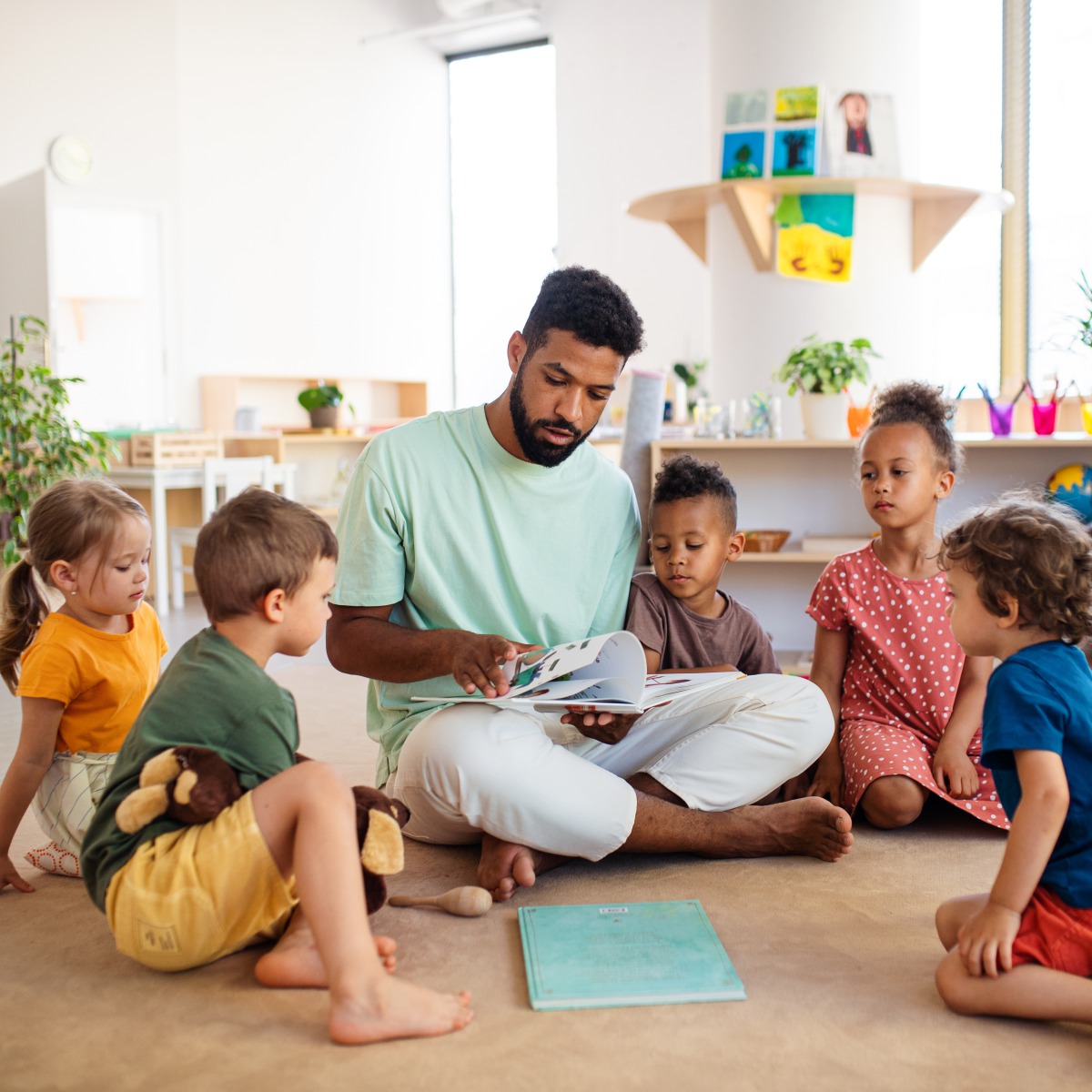 Kita Nordmännchen – Geschichtenzeit mit Herz 💛 Ein männlicher Erzieher liest einer Gruppe Kinder im Sitzkreis in der Kita Nordmännchen vor – gebanntes Zuhören, Geborgenheit, Interaktion.